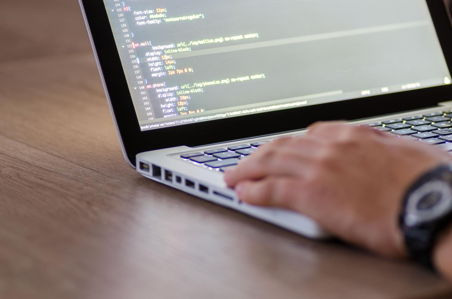 Desarrollador programando en un portátil con un reloj de pulsera, simbolizando la gestión del tiempo en el desarrollo web.