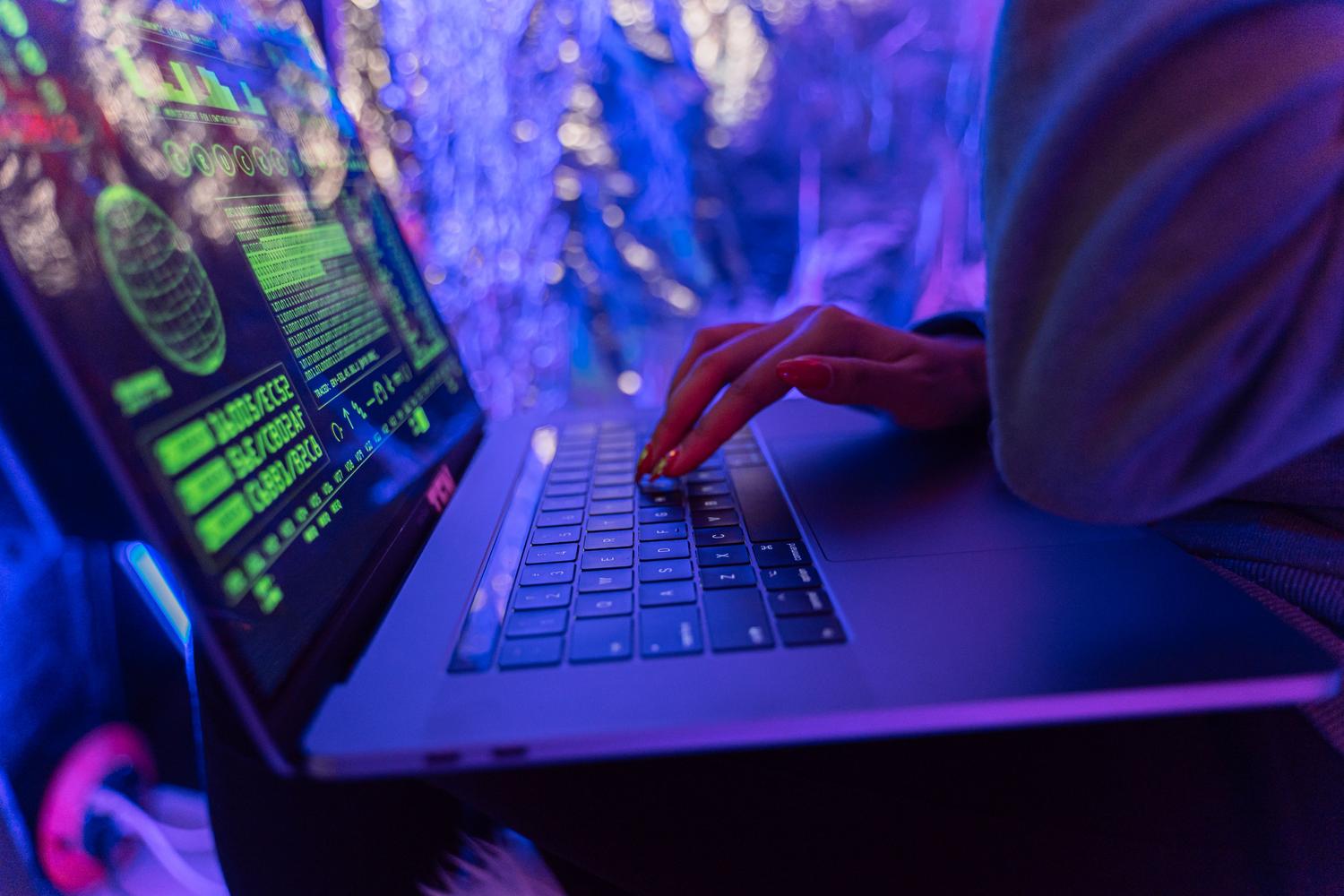 Primer plano de manos escribiendo en un portátil con gráficos digitales de ciberseguridad.