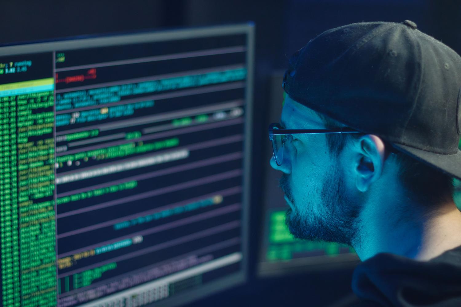 Experto en seguridad analizando líneas de código en múltiples monitores, simbolizando la protección y monitorización del sistema.