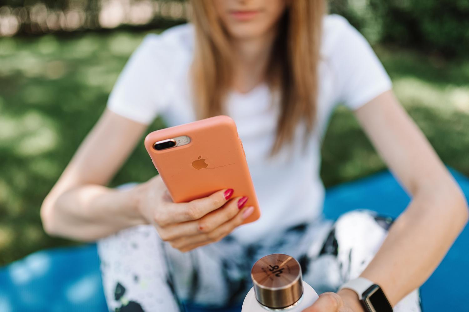 Persona utilizando un iPhone y llevando un Apple Watch en un entorno exterior, ilustrando el uso de dispositivos vinculados.