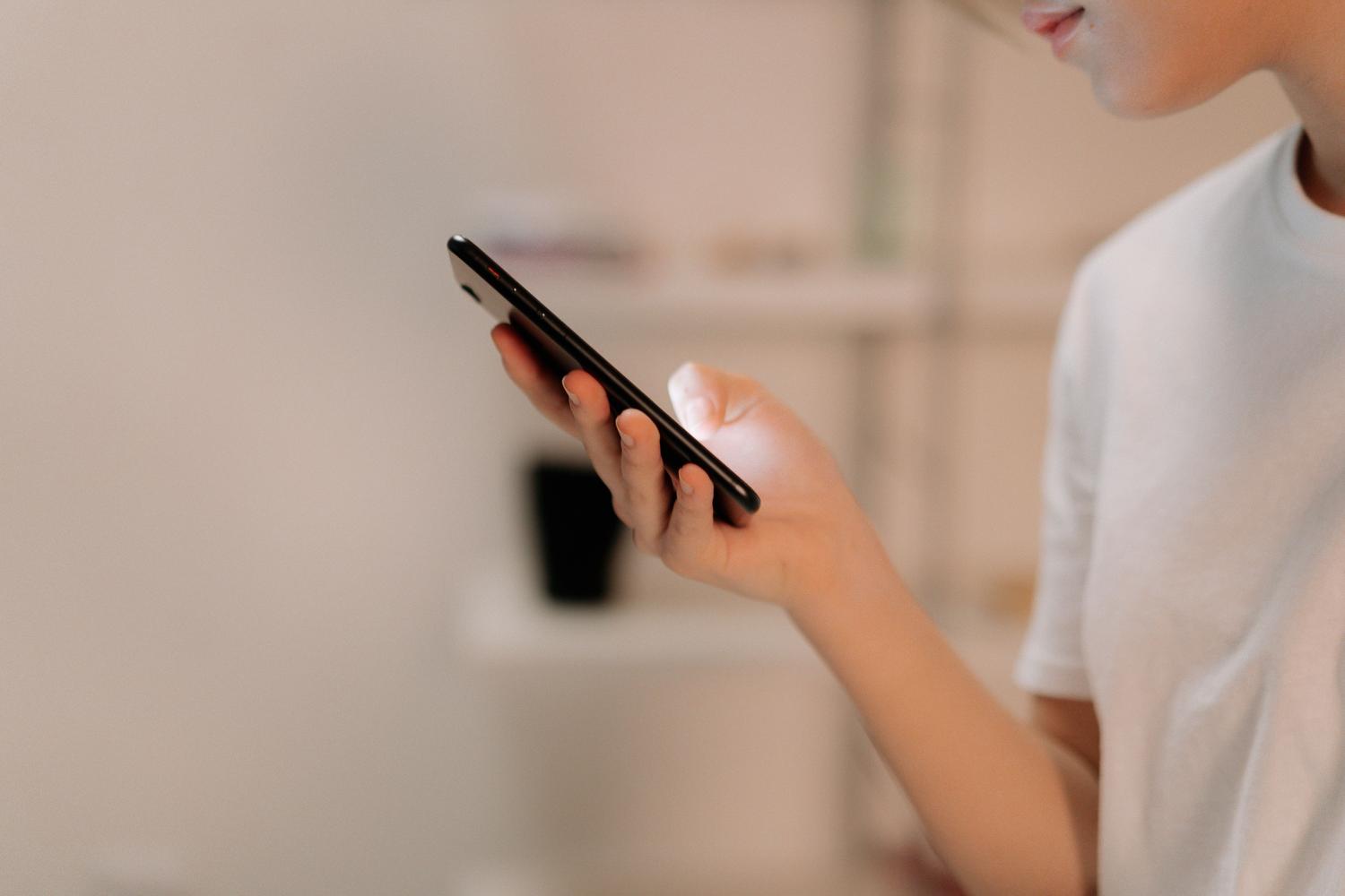 Primer plano lateral de una mano sosteniendo un iPhone, representando el uso cotidiano del dispositivo.
