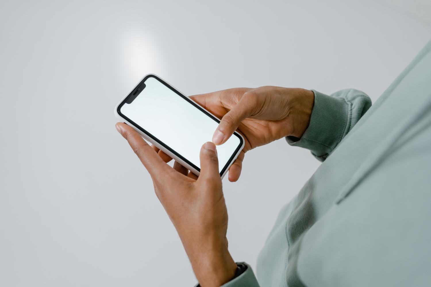 Primer plano de una persona utilizando un iPhone con pantalla en blanco, ideal para ilustrar la búsqueda de datos o configuración técnica.