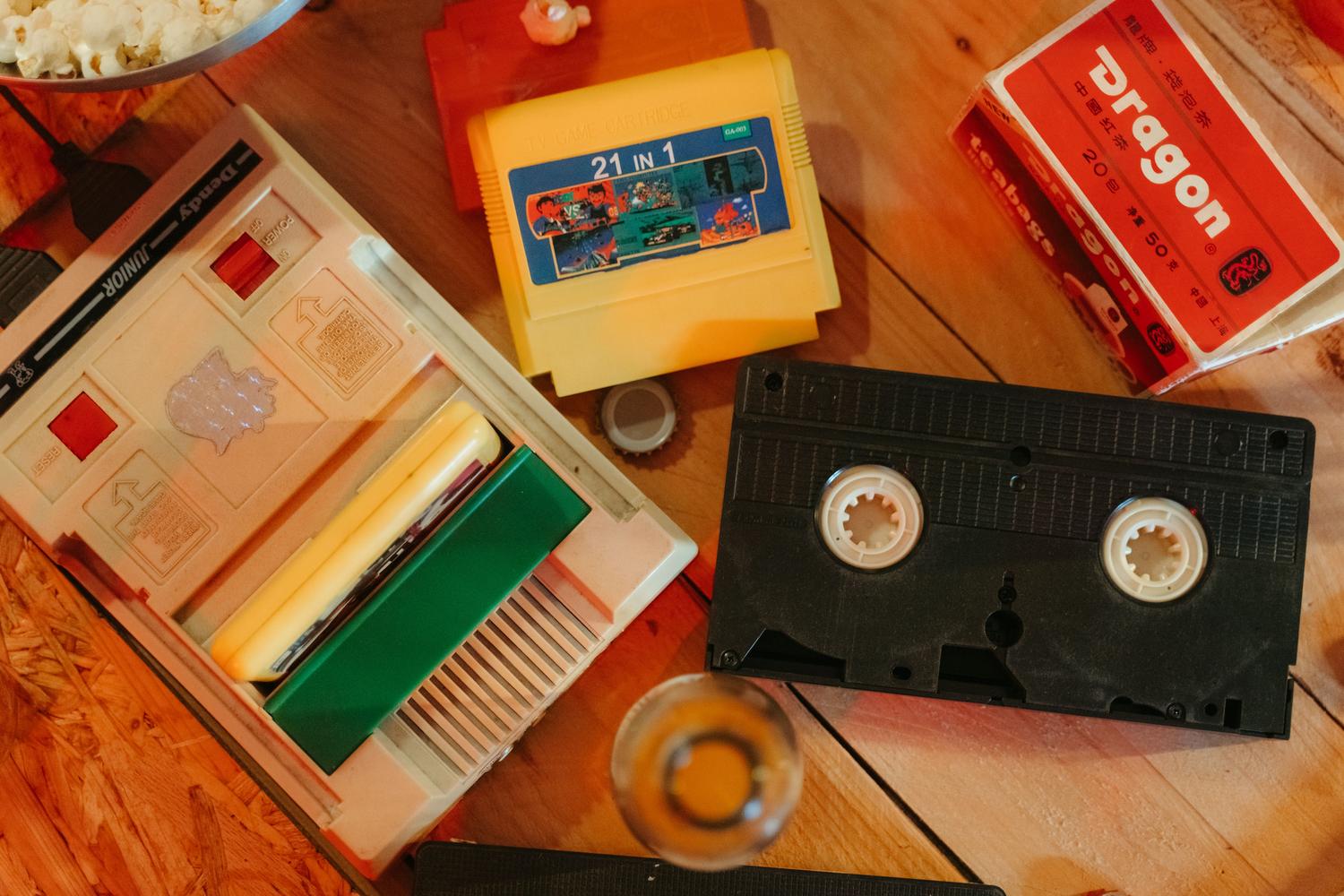 Consola de videojuegos vintage con cartuchos y cinta VHS sobre una superficie de madera, evocando la nostalgia de los años 80.
