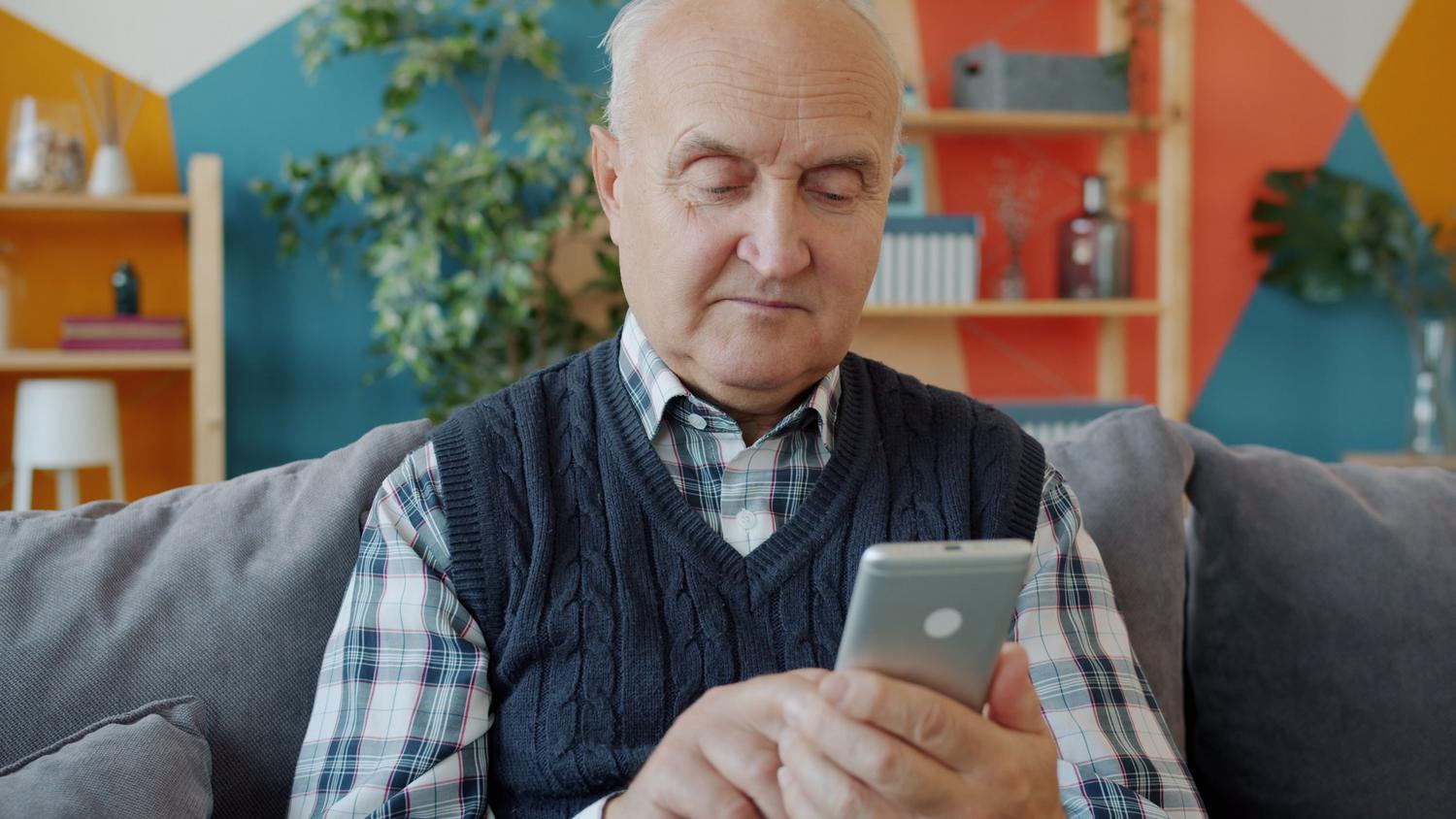 Persona mayor utilizando un smartphone en su hogar, ilustrando la vulnerabilidad de este grupo demográfico ante consejos médicos falsos en redes sociales.