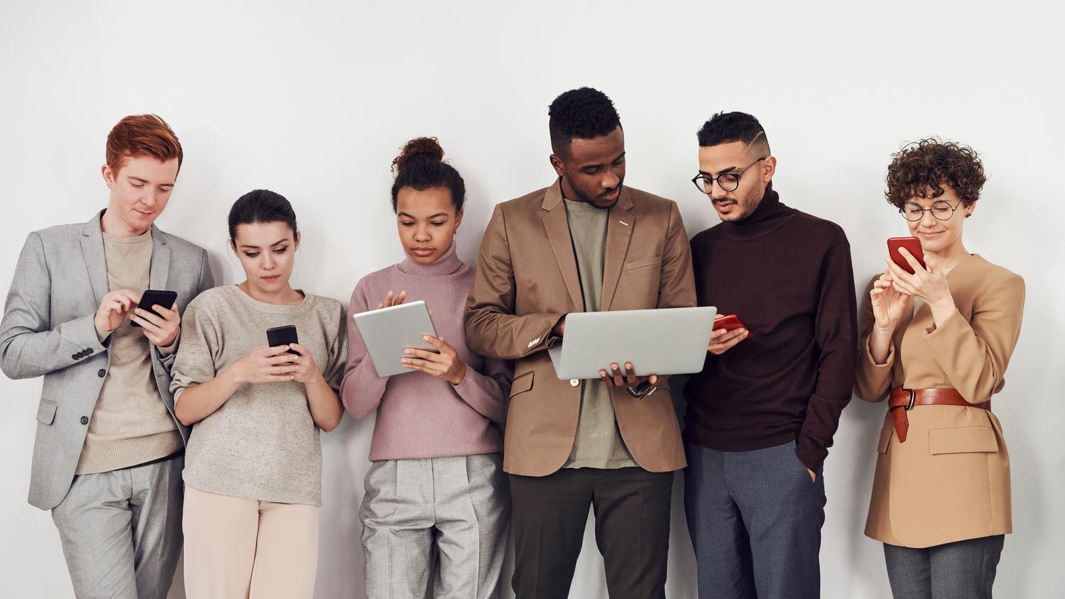 Grupo diverso de jóvenes profesionales utilizando laptops y smartphones, representando la red de contactos y el público objetivo de LinkedIn.