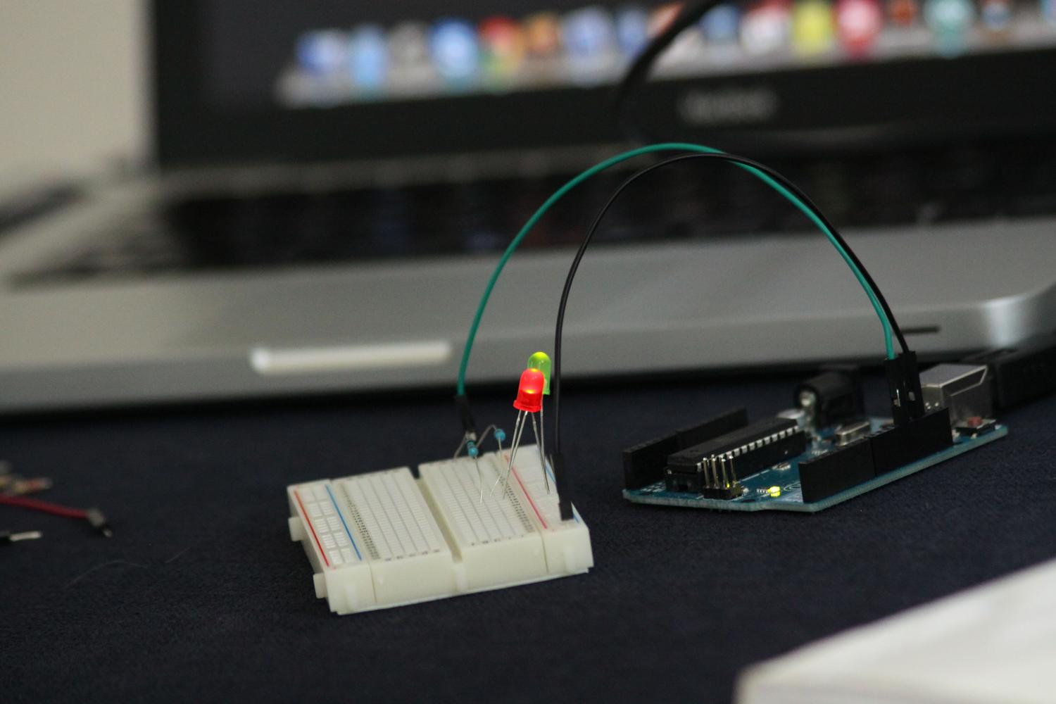 Setup de microcontrolador con LEDs en una protoboard junto a un ordenador portátil, representando la relación entre el código y el hardware.