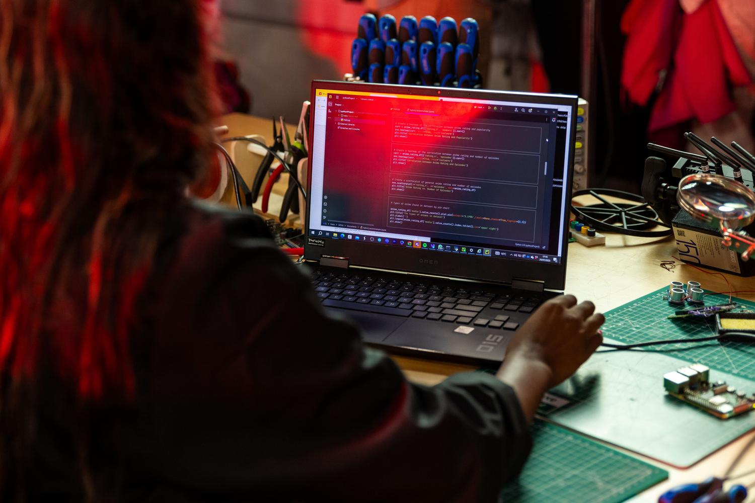 Programador escribiendo código en un portátil rodeado de herramientas y componentes electrónicos