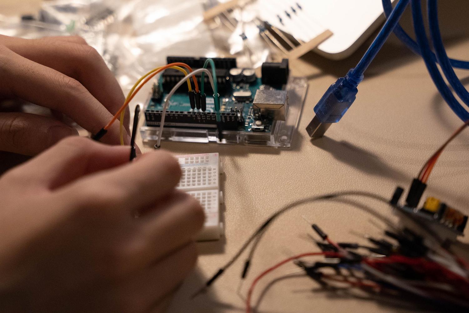 Primer plano de manos conectando cables jumper en un circuito electrónico con Arduino