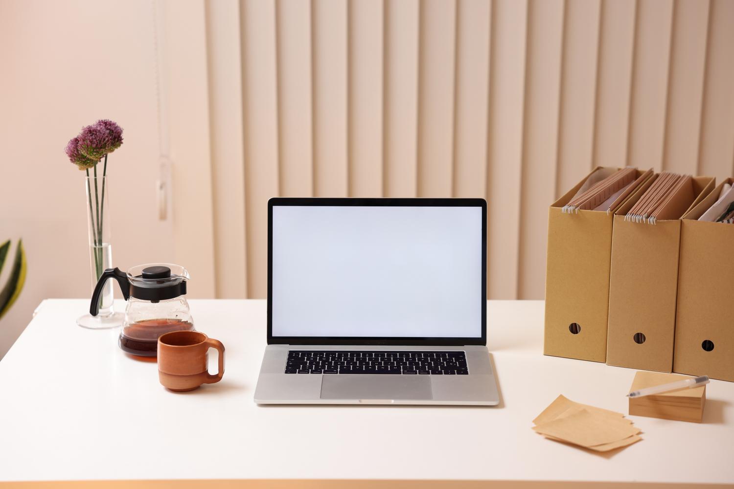 Espacio de trabajo minimalista con un portátil y organizadores de archivos, simbolizando la organización y limpieza de archivos digitales.