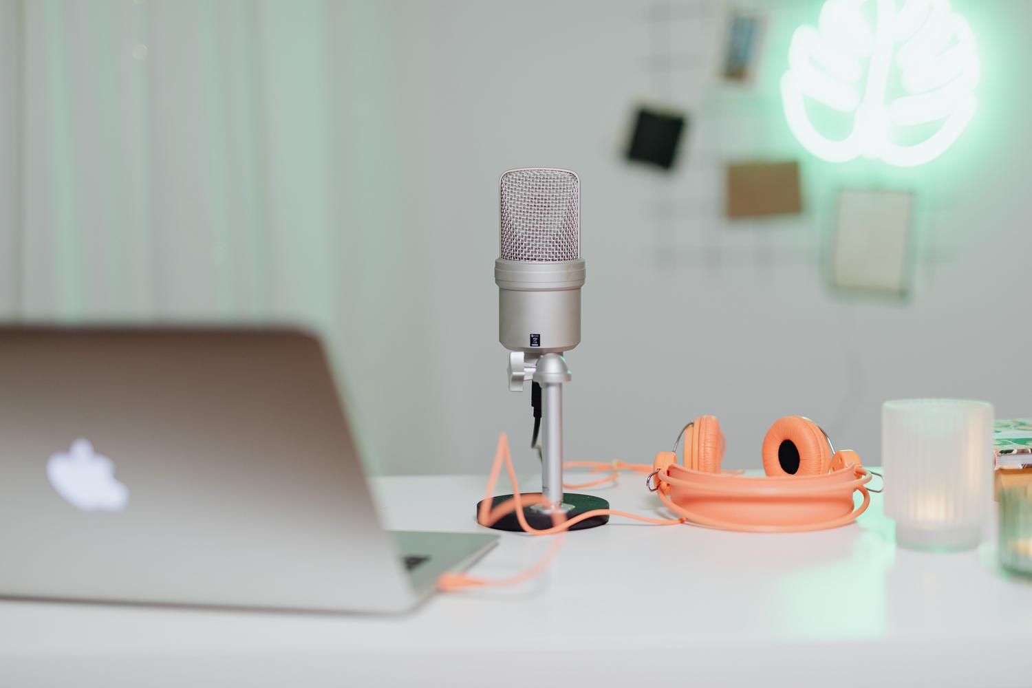 Escritorio de trabajo minimalista con micrófono de condensador, portátil y auriculares.