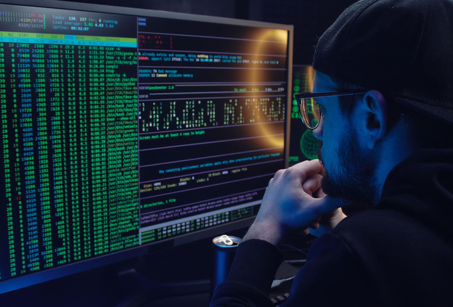 Analista de seguridad trabajando en un entorno oscuro con múltiples monitores mostrando código y datos de sistema