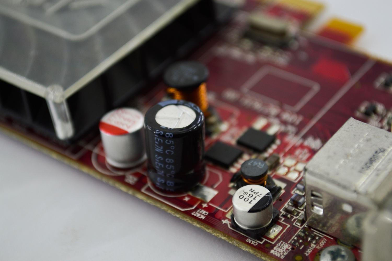 Fotografía detallada de condensadores y trazados de cobre sobre una placa base de color rojo, ilustrando la ingeniería electrónica.